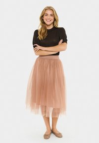 Top corto nero a maniche corte abbinato a una gonna midi in tulle di un rosa pallido. La gonna presenta una vita aderente e un design a strati; le scarpe sono decorate con borchie.