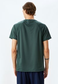 Kortärmad atletisk tröja i mörkgrön färg, gjord av ett glansigt och lätt tyg. Har raglanärmar och en enkel, ren design.