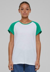 Hvit t-skjorte med grønne raglan-ermer, rund hals og korte ermer. Mykt stoff med avslappet passform, kombinert med blå jeans.