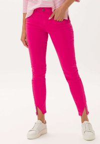 Jeans de mezclilla rosa con corte ajustado, que presentan aperturas laterales en el dobladillo, combinados con zapatillas blancas. La tela parece suave y elástica.