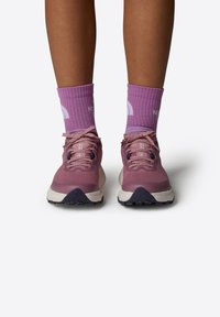 Zapatillas deportivas moradas con parte superior de tejido, cordones rosas, entresuela blanca en contraste y suela negra. Combinadas con calcetines morados a juego.