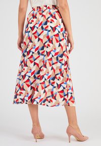 Jupe longue à motif en beige avec des formes géométriques rouges, bleues et blanches. Dotée d'une taille élastique et d'une silhouette fluide.