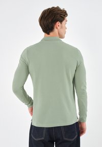 Langærmet polo-shirt i lysegrøn, lavet af blødt stof, har en klassisk krave og er parret med mørk denim jeans.