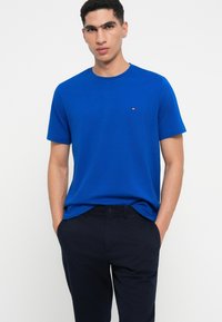 Karaliski zils īsā piedurkne T-krekls ar apaļu kakla izgriezumu un mazu logotipa detaļu uz krūtīm, apvienots ar tumši ziliem biksēm.