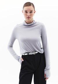 Lichtgrijs langemouw turtleneck-shirt met een zachte structuur, gecombineerd met zwarte high-waisted broeken en een riem met zilveren gesp.