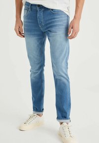 Ljust blå jeans med slim fit, som har en klassisk femficksdesign, subtila blekningar och uppvikta fållar, i kombination med vita sneakers.