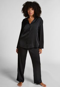 Zwart satijnen pyjama-set met een knoopsluiting, lange mouwen, een borstzakje en bijpassende wijde broek met subtiele verticale strepen.