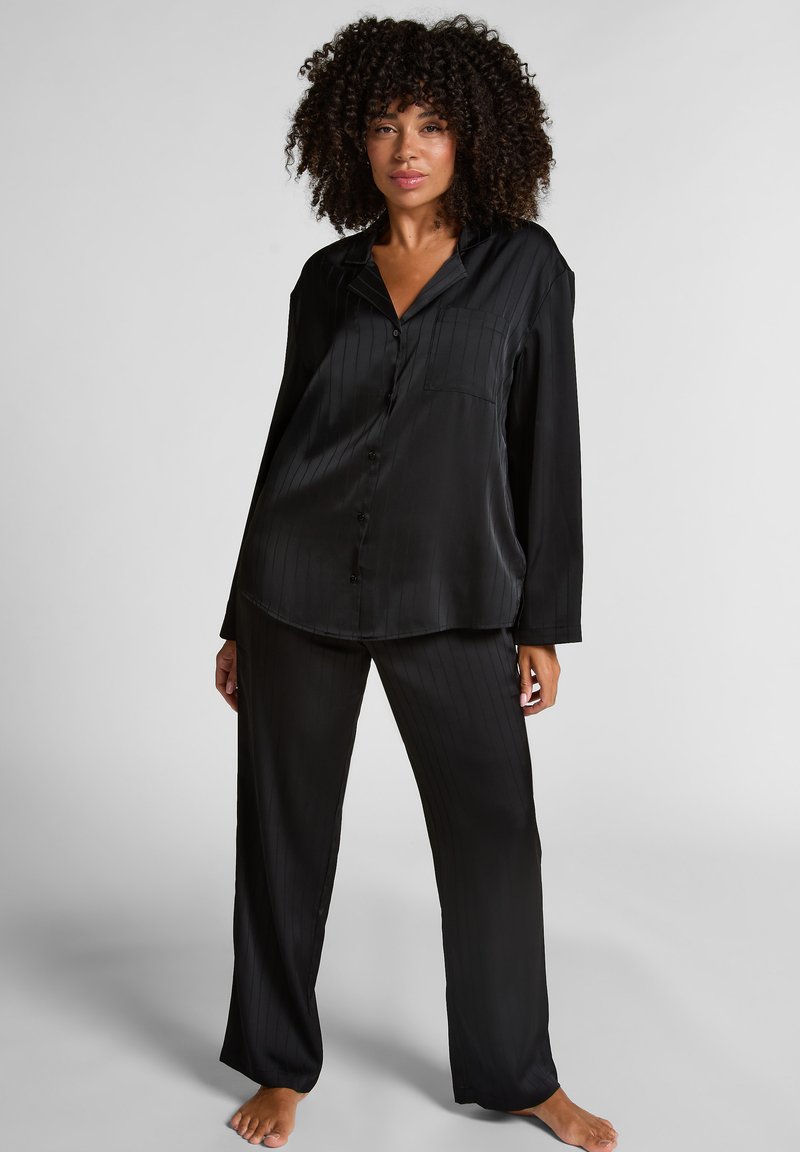 Zwart satijnen pyjama-set met een knoopsluiting, lange mouwen, een borstzakje en bijpassende wijde broek met subtiele verticale strepen.