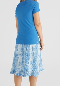 Top azul de manga corta con escote redondo, combinado con una falda fluida que presenta un patrón abstracto en azul y blanco y dobladillo con volantes.