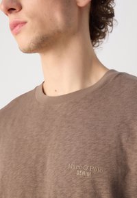 Brown cotton t-shirt featuring a ribbed crew neckline and subtle "Marc O'Polo DENIM" logo in light beige on the front.