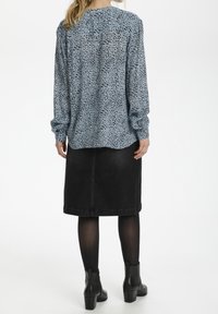 Blå mønstret bluse med sorte pletter, lange ærmer og høj hals, parret med en sort denimnederdel, båret med sorte ankelstøvler.