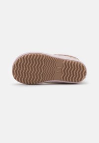 Semelle de sneaker en beige avec une texture en zigzag, en matériau en caoutchouc et de forme arrondie. Comprend un petit détail de logo.