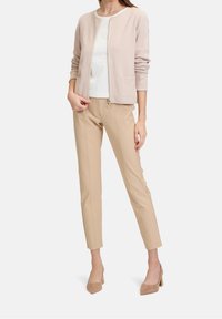 Světle růžová zipová bunda s dlouhými rukávy, v kombinaci s béžovými slim-fit kalhotami a béžovými lodičkami. Jednoduchý design bez vzorů či akcentů.