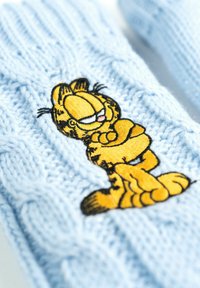 Muffole lavorate a maglia di colore azzurro chiaro con un design ricamato di un gatto cartoon arancione e nero in una posa rilassata, con dettagliati tratti del viso.