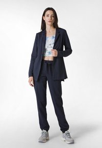 Marinblå avslappnad kostym med en åtsittande jacka och lösa byxor. Åtföljs av en ljusblå tie-dye crop top och grå sportskor.