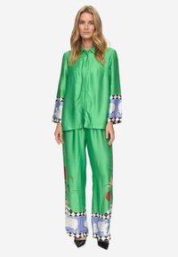 Set di abbigliamento da casa in raso verde composto da camicia con bottoni e pantaloni a gamba larga. Maniche decorative con motivi floreali e orli a contrasto.