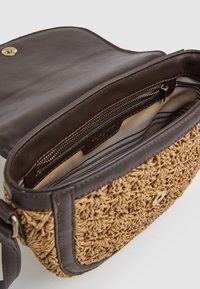 Brązowa skórzana torebka na ramię z plecionego słomkowego materiału, z zamykaną na zamek kieszenią i paskiem z prążkowanej tkaniny. Posiada metalowe zapięcie na zatrzask.