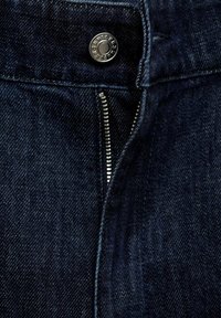 Acercamiento de unos jeans de mezclilla en un tono azul oscuro, con una cremallera metálica parcialmente abierta y un botón plateado en la cintura.