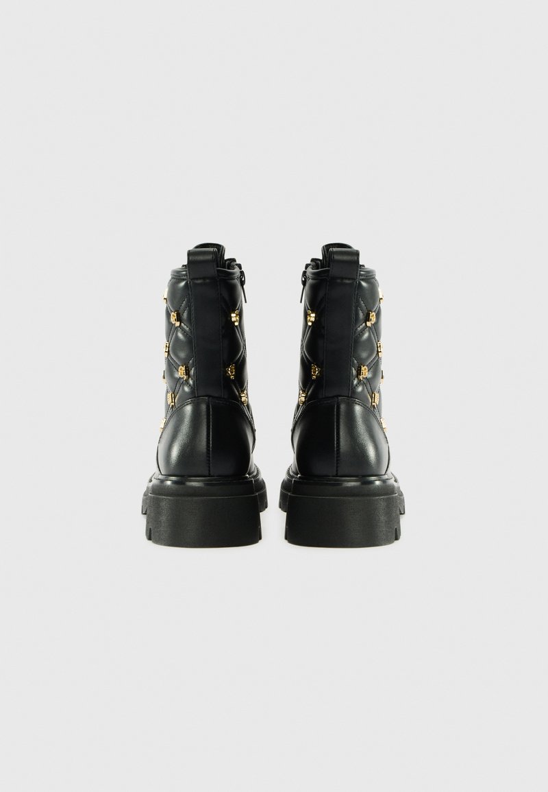 Zwarte leren enkelboots met een gequilt ontwerp en accenten in goudkleurig hardware, voorzien van een chunky zool en ritssluiting aan de achterkant.
