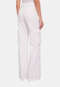 Pantaloni cargo bianchi con gamba larga, dotati di due tasche posteriori e tasche laterali cargo. Realizzati in tessuto leggero con una texture liscia e una vestibilità sartoriale.