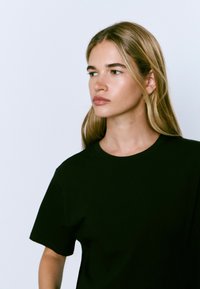 T-shirt en coton noir avec un col rond et des manches courtes, présentant une coupe décontractée et une texture douce. Design simple, sans motifs ni accents.