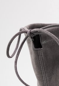 Botín de ante gris hasta el tobillo con puntera redondeada, detalle de corte y lazada atada en la apertura. Textura suave con costuras visibles.