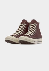 Ζευγάρι από σκουροκόκκινα κοντινά παπούτσια από καμβά με λευκά κορδόνια και λαστιχένιες σόλες, τοποθετημένα γωνιακά προς τα δεξιά σε λευκό φόντο.