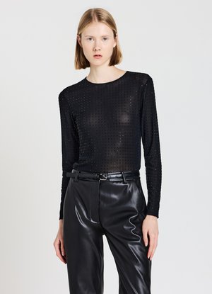 Schwarzes Langarmoberteil aus transparenter Stoff mit strukturiertem Punktenmuster, kombiniert mit hoch taillierten schwarzen Kunstlederhosen und einem schmalen Gürtel.