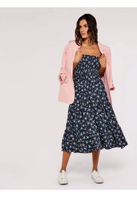 Marineblaues Blumen-Midi-Kleid mit gerafftem Oberteil, ausgestelltem Rock und kurzen Spaghetti-Trägern, kombiniert mit einem hellrosa Blazer und weißen Turnschuhen.