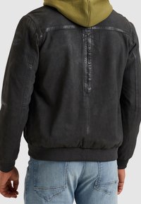 Zwarte leren jas met geribbelde manchetten en zoom, met een gladde textuur, een olijfgroene hoodie eronder en subtiele merkdetails.