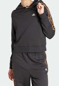 Černá zkrácená mikina s kapucí a šňůrkou, s oranžovými vzorovanými pruhy na rukávech a logem Adidas na hrudi.