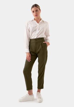 Olijfgroene broek met geplooide voorkant, hoge taille en zijzakken. Gepaard met een wit overhemd met knopen en witte sneakers.