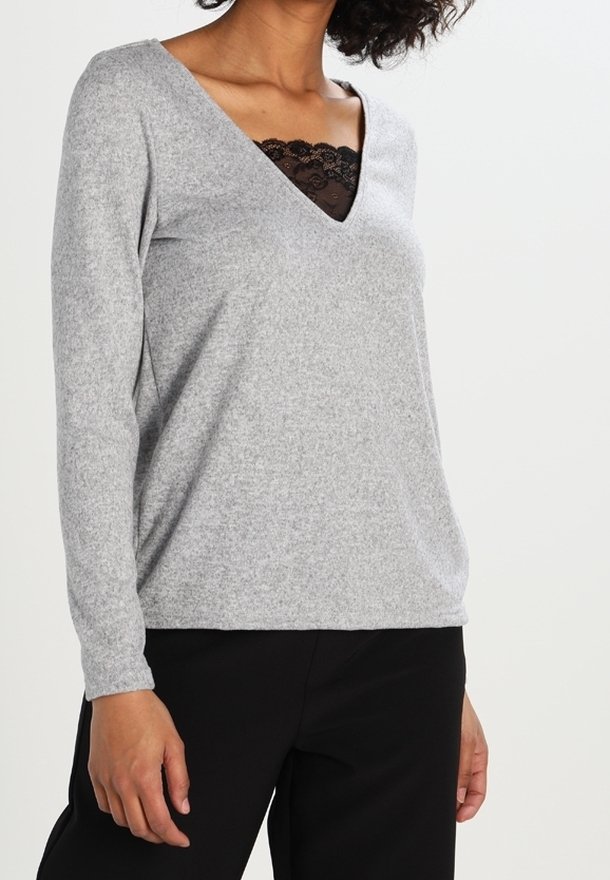 Graues Longsleeve-Oberteil mit V-Ausschnitt, unter dem sich ein schwarzes Spitzen-Detail befindet. Der Stoff hat ein weiches, strukturiertes Aussehen.