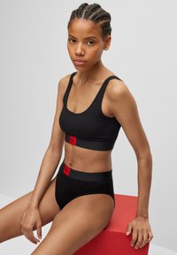 Black cotton sports bra and high-waisted underwear set featuring red logo bands, with a smooth texture and minimalistic design.