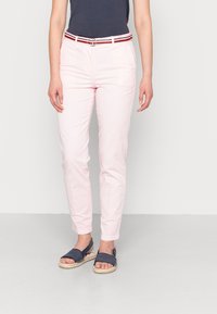 Světlé růžové kalhoty se slim fit a obroubenými lemy, s bílým, červeným a černým proužkovaným opaskem. Nosí se s námořnickými espadrilkami.