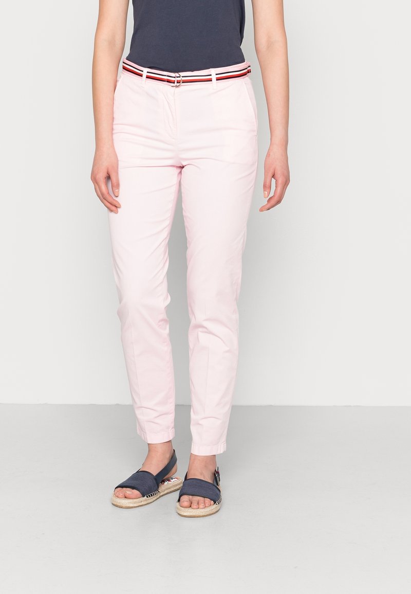Světlé růžové kalhoty se slim fit a obroubenými lemy, s bílým, červeným a černým proužkovaným opaskem. Nosí se s námořnickými espadrilkami.