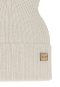 Beige gebreide muts met geribbelde textuur, voorzien van een opgevouwen boord en een klein leren label met de tekst "LESS IS MORE".