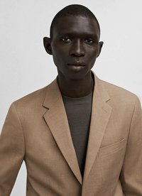 Bežna lanena blejzerica z notčastim ovratnikom, eno žepom in temno rjavim puloverjem z okroglim ovratnikom pod njo. Gladka tekstura, čiste linije.