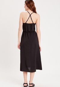 Robe noire midi avec une taille cintrée, dotée de bretelles croisées et d'une jupe fluide. Fabriquée en tissu léger avec une texture douce.