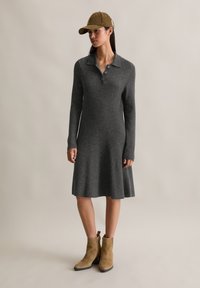 Abito grigio a coste con colletto, maniche lunghe e gonna svasata, abbinato a stivali in suede beige con cerniera alla caviglia e a un cappello kaki.