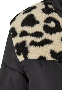 Gevoerde zwarte jas met een beige en zwarte gebreide yoke met een gekorrelde afwerking, in contrast met de gladde stof eronder.