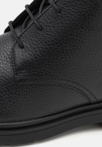 Botte en cuir noir avec surface texturée, bout rond et couture renforcée. Comprend des lacets noirs et une semelle en caoutchouc épaisse.