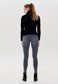 Schwarzer gerippter Rollkragenpullover kombiniert mit grauen engen Jeans. Die Jeans haben Gesäßtaschen und eine glatte, dehnbare Textur. Schwarze Absatzstiefel sind sichtbar.