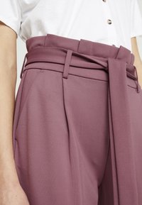 Kalhoty s vysokým pasem v barvě švestky s širokým vázacím páskem, ve přední části sklady a hladkým, texturovaným materiálem. Ležérní design.