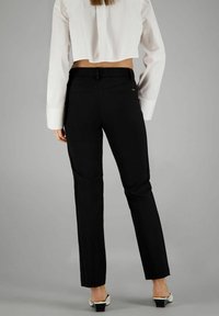 Schwarze maßgeschneiderte Hose mit geradem Schnitt, ausgestattet mit Gesäßtaschen und einem glatten Stoffoberfläche. Kombiniert mit einem weißen, kurz geschnittenen Hemd.