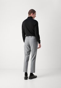 Grå bukser med en skreddersydd design, baklommer og smal passform, kombinert med en svart langermet topp og mørke sko.