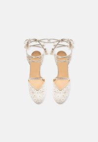 Coppia di sandali espadrillas beige in pizzo con cinturini intrecciati alla caviglia e nappine, motivo floreale nella zona delle dita, suola piatta.