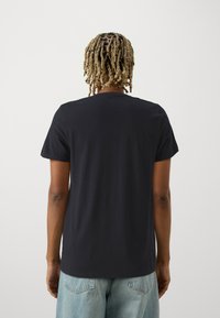 Schwarzes, kurzärmliges T-Shirt aus Baumwolle mit Rundhalsausschnitt und lockerer Passform, von hinten gezeigt, kombiniert mit blauen Jeans.
