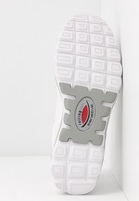 Semelle de chaussure blanche avec des crampons carrés et un patch gris étiqueté "rollingsoft sensitive" avec un design rouge et noir.