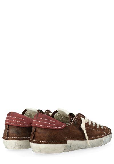 Sneaker in suede marrone con suole in gomma bianca, linguette sul tallone rosse a contrasto e lacci color crema con dettagli di cucitura visibili.